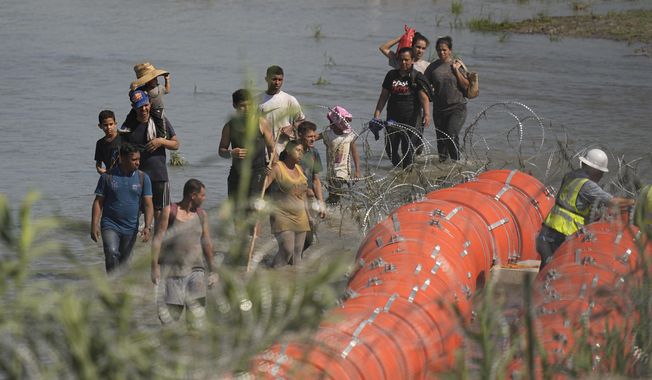 Migrants trying to enter the U.S. from Mexico approach the site where workers are assembling large buoys to be used as a border barrier along the banks of the Rio Grande in Eagle Pass, Texas, Tuesday, July 11, 2023. The floating barrier is being deployed in an effort to block migrants from entering Texas from Mexico. (AP Photo/Eric Gay)