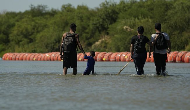 Migrants crossing into the U.S. from Mexico walk along large buoys being used as a floating border barrier on the Rio Grande Tuesday, Aug. 1, 2023, in Eagle Pass, Texas. (AP Photo/Eric Gay)