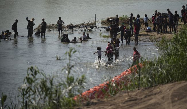 Migrants cool themselves in the waters of the Rio Grande after crossing to the U.S. from Mexico near a site where the state is installing large buoys to be used as a border barrier along the Rio Grande near Eagle Pass, Texas, Monday, July 10, 2023. (AP Photo/Eric Gay)